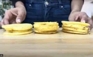 Sliced potatoes on a wooden board, ready for cooking. Close-up of hands arranging the thin potato slices.